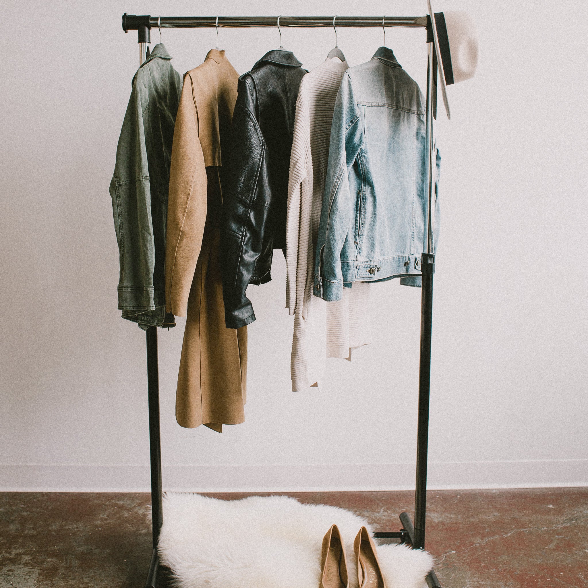 Blonde woman with a minimalist style, wearing a brown coat, a black T-shirt and light blue jeans, carrying a classic black handbag.