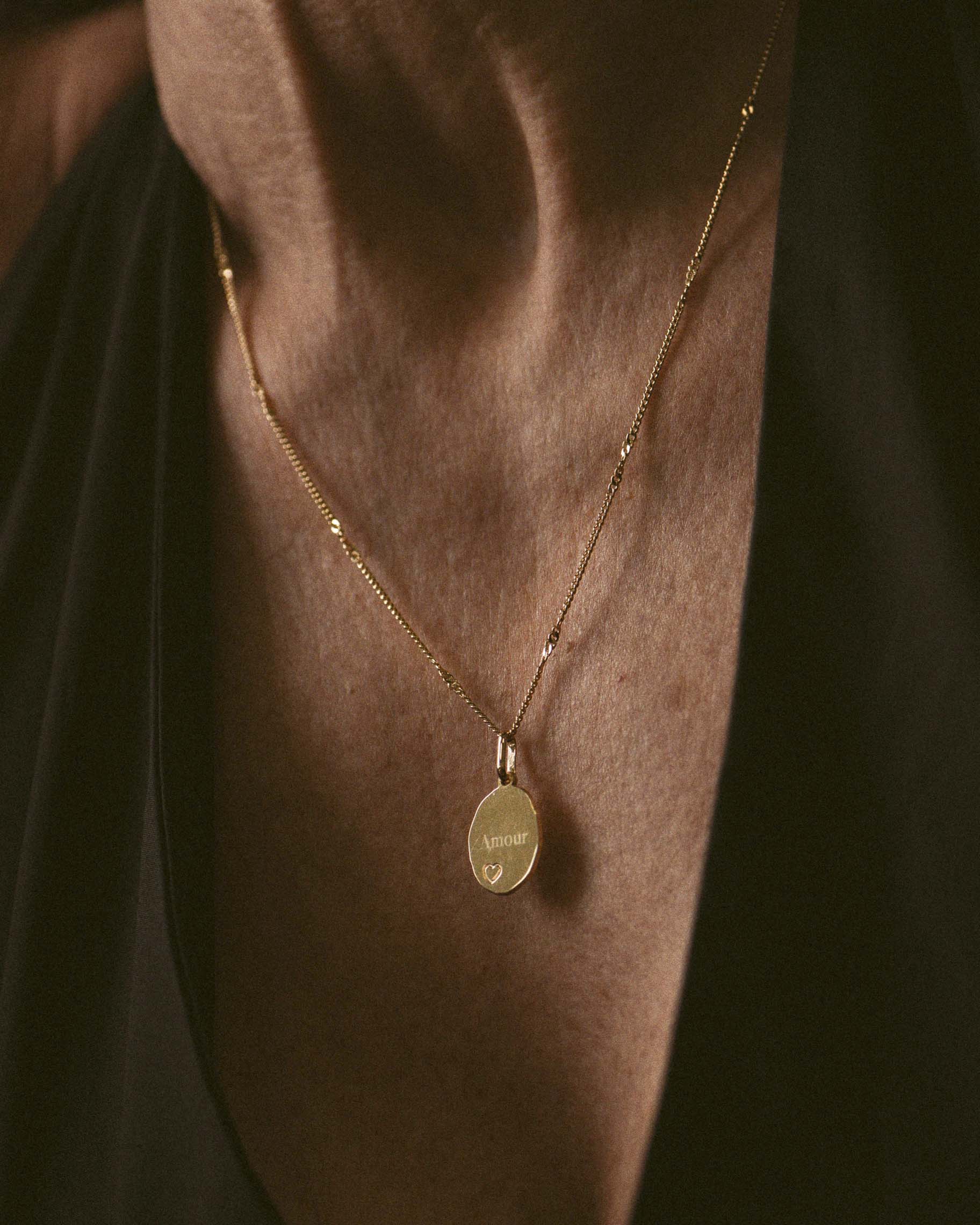 Collier en chaîne torsadée avec un pendentif en médaille ovale avec un motif cœur et le mot Amour gravé, fabriqué en France.