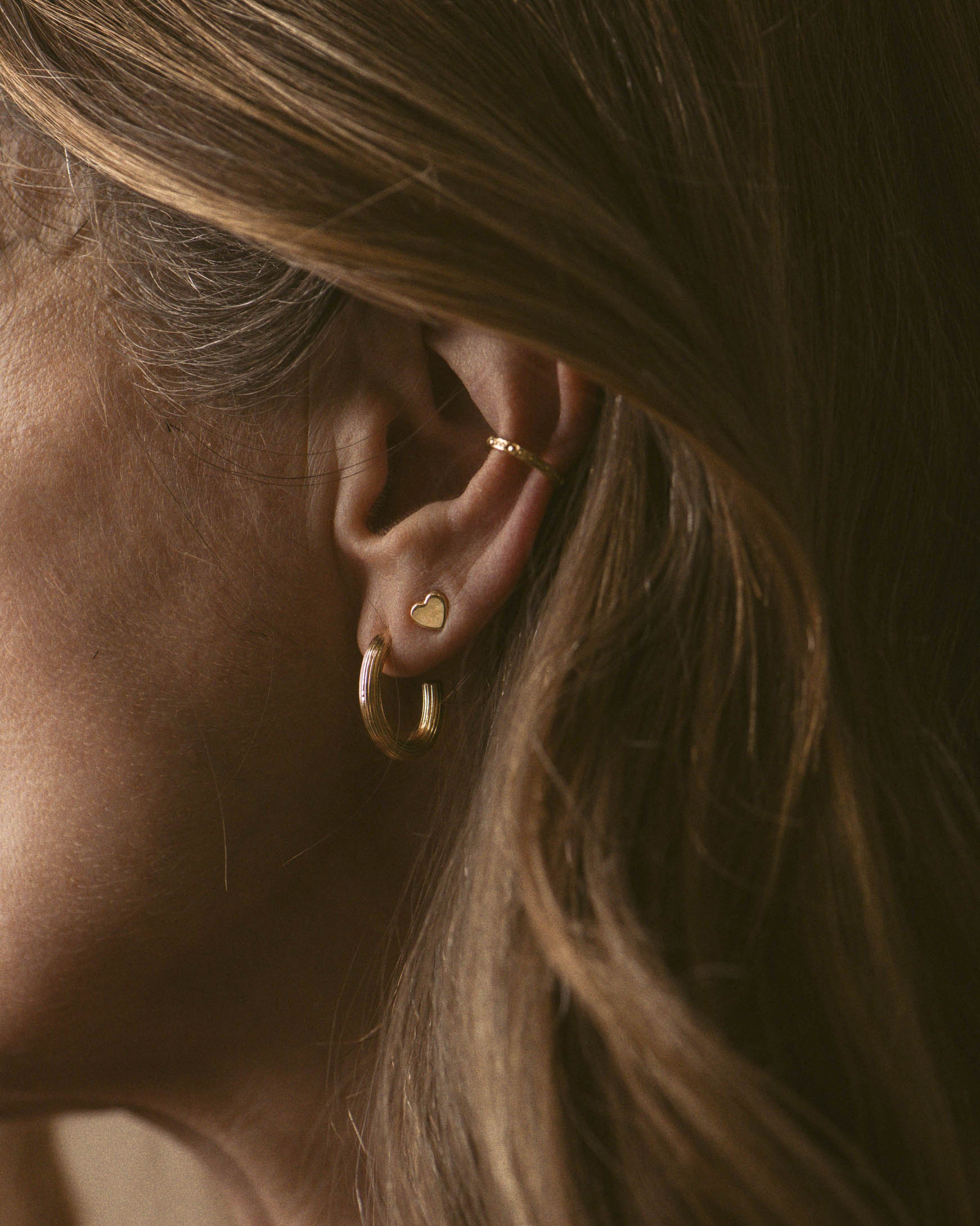 Bijoux en plaqué or composés d'une petite boucle en puce en forme de cœur, d'un anneau d'oreille fin, et d'une créole aux motifs striés, fabriqués en France.