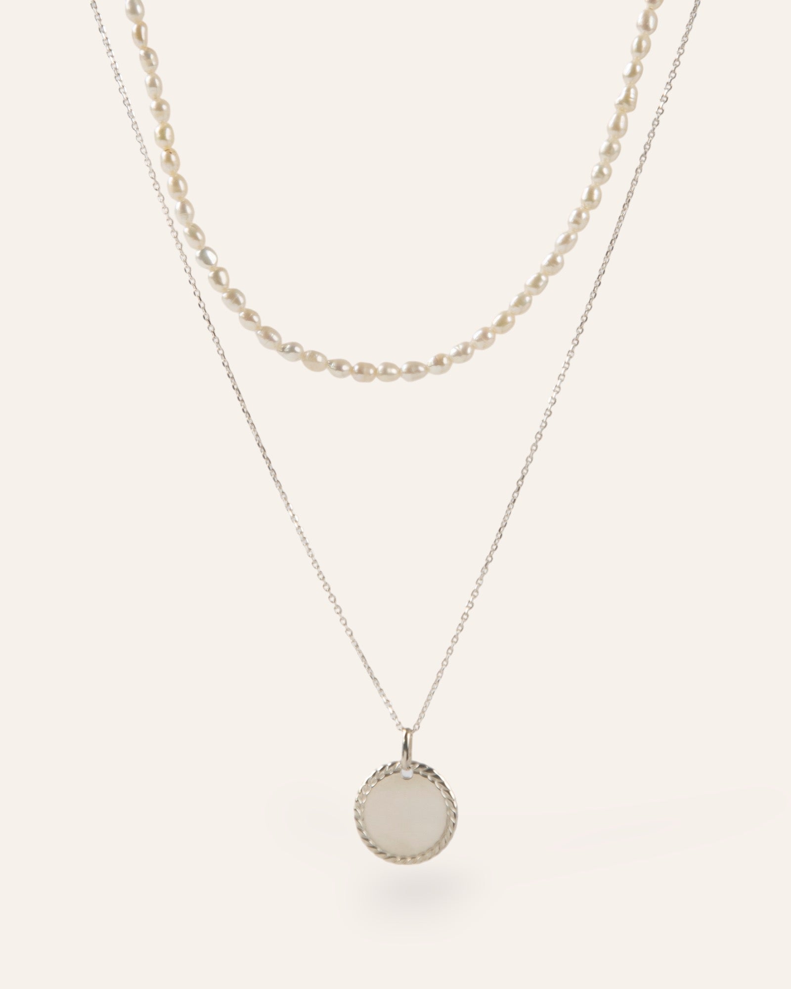 Composition de deux colliers, avec un collier orné de perles de culture, et un collier en chaîne forçat avec une médaille torsadée en argent massif 925 made in France.