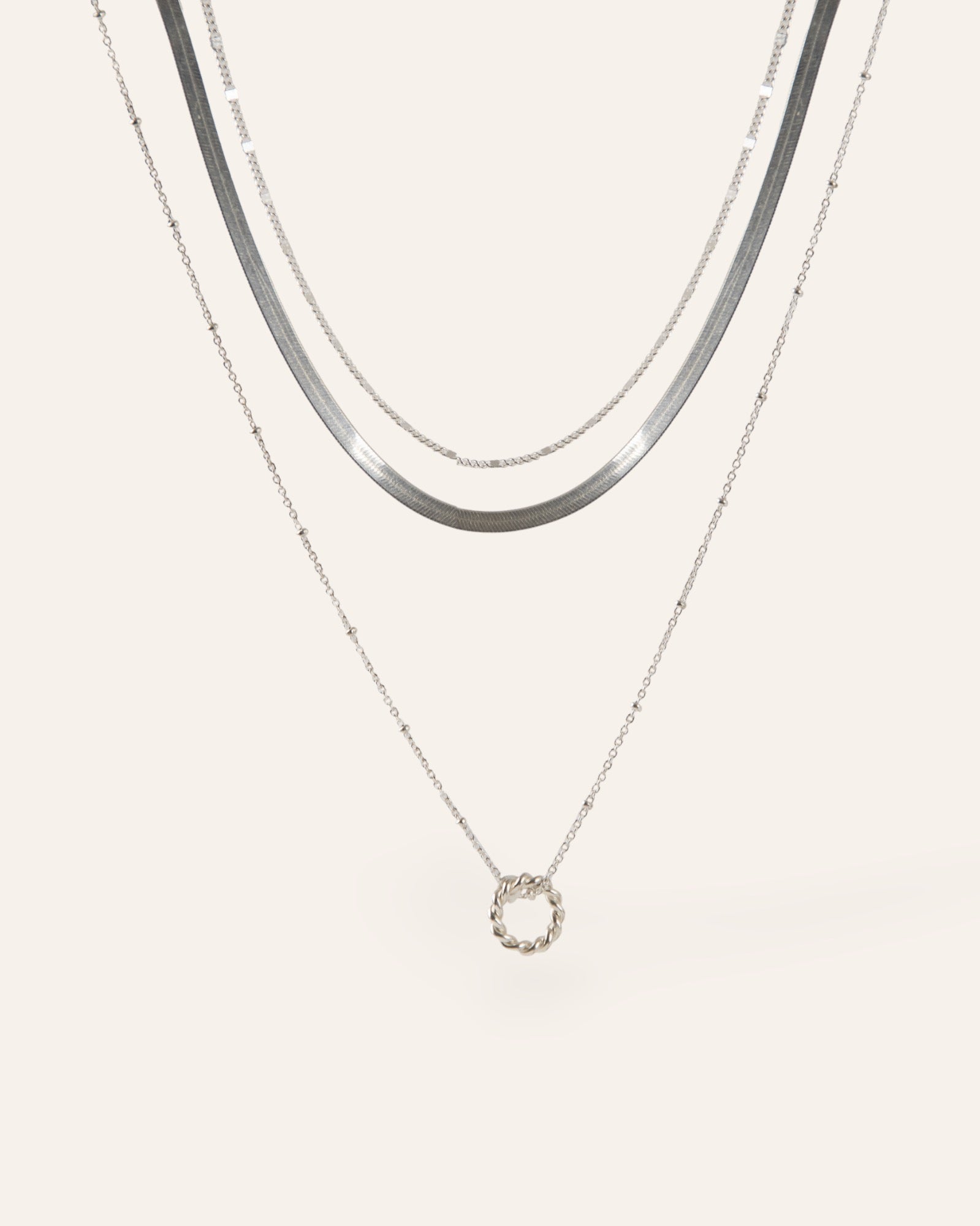Composition de trois colliers, avec un collier en chaîne plate, un collier en chaîne de type gourmette, et un collier en chaîne boule avec un pendentif en anneau torsadé, en argent massif 925 made in France. 