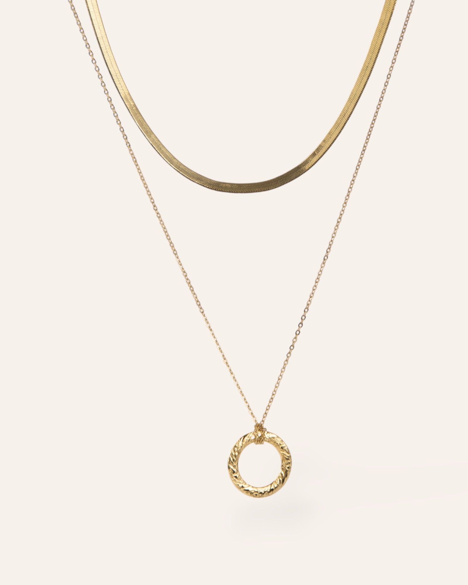Composition de deux colliers, avec un collier en chaîne plate et un collier en chaîne forçat avec un pendentif en anneau plat texturé au motif de style vintage, en plaqué or 18 carats.