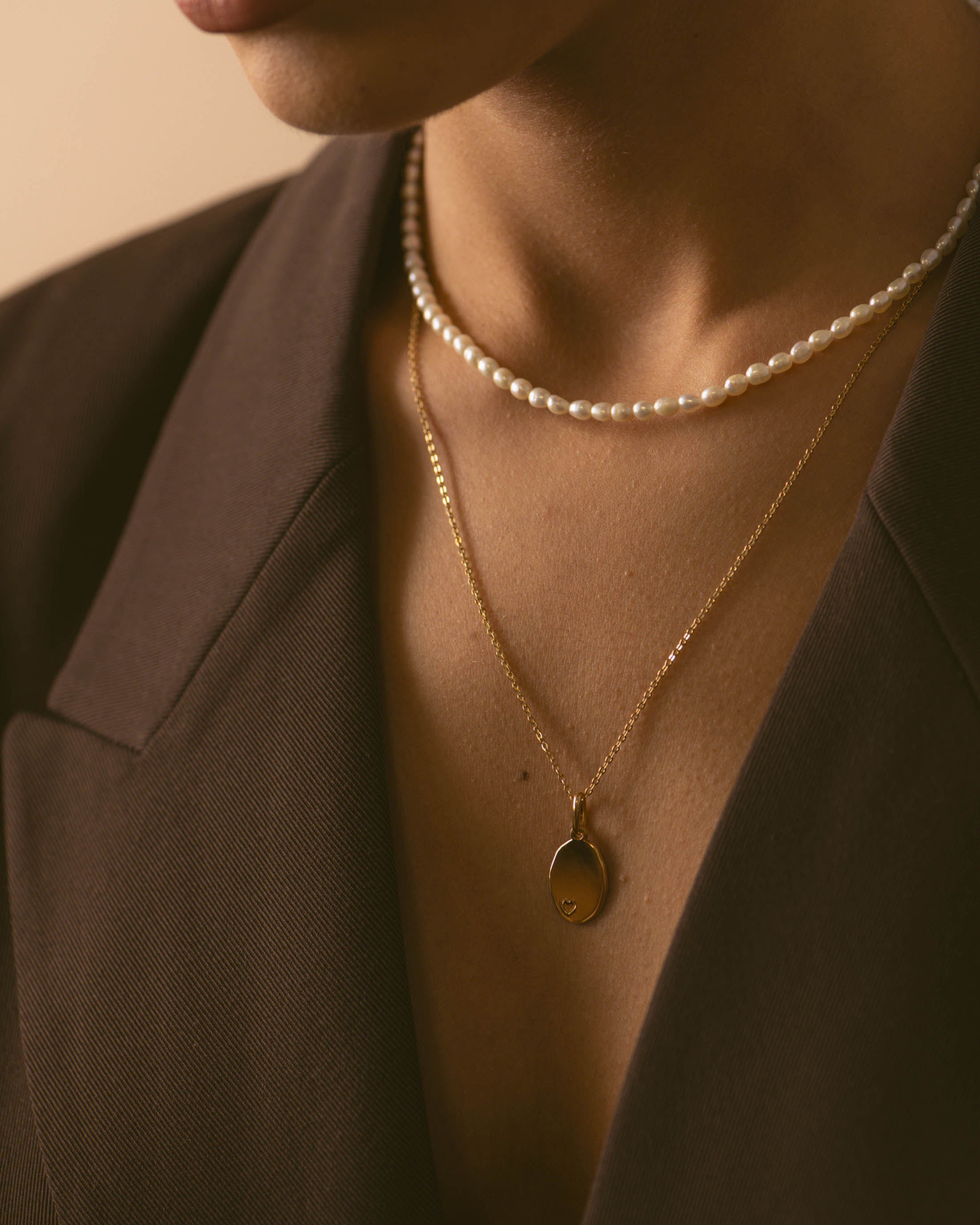 Association de colliers en plaqué or 18 carats, composée d'un collier en perles de culture et d'un collier en chaîne forçat avec un pendentif ovale avec un petit coeur en motif made in France. 