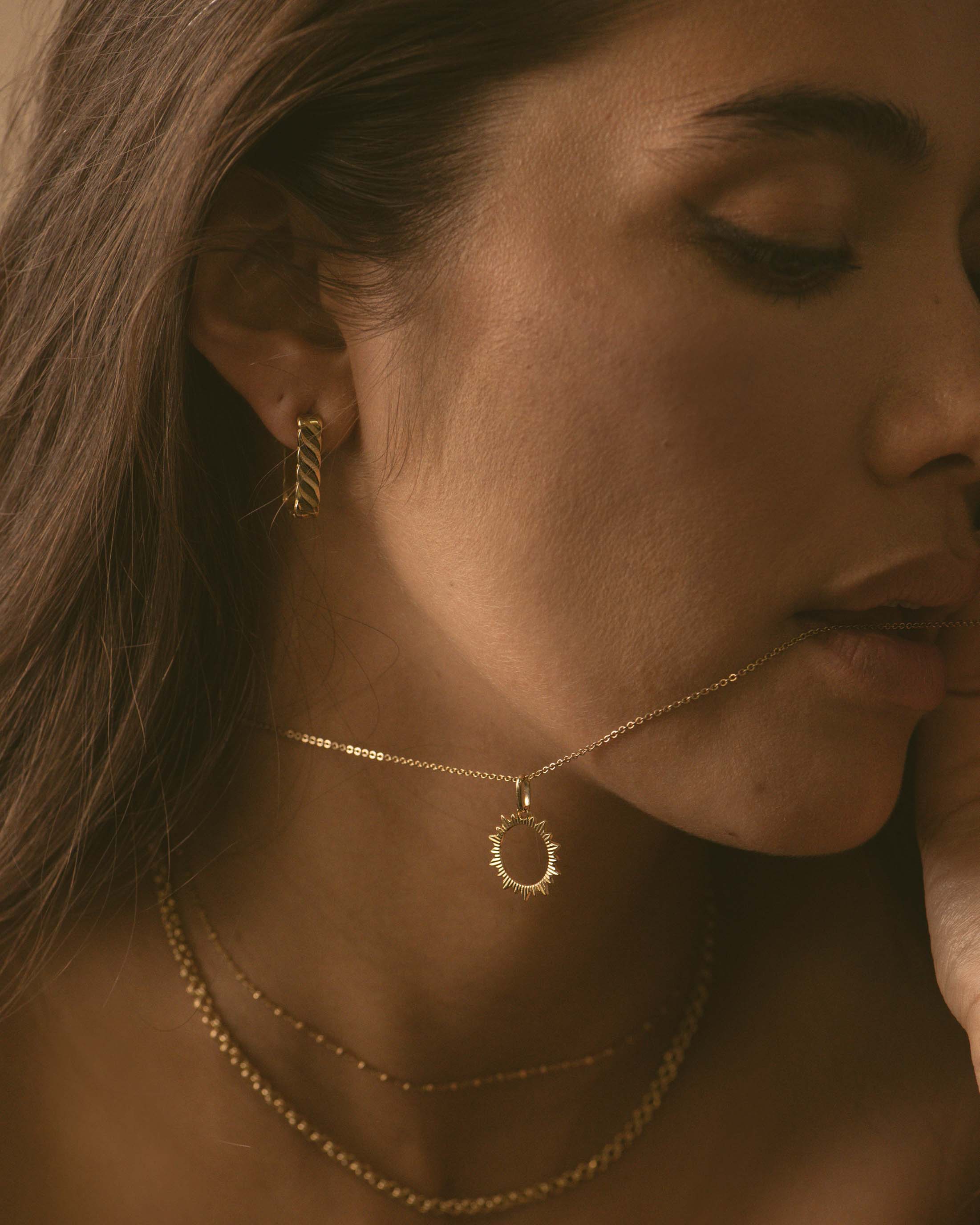 Conjunto de joyas sostenibles: un pendiente rectangular con diseño ondulado, un collar con colgante de sol calado, un choker con pequeñas eslabones cuadrados y un collar de cadena forzada con eslabones redondos, chapado en oro de 18 quilates (3 micras), fabricado en Francia.