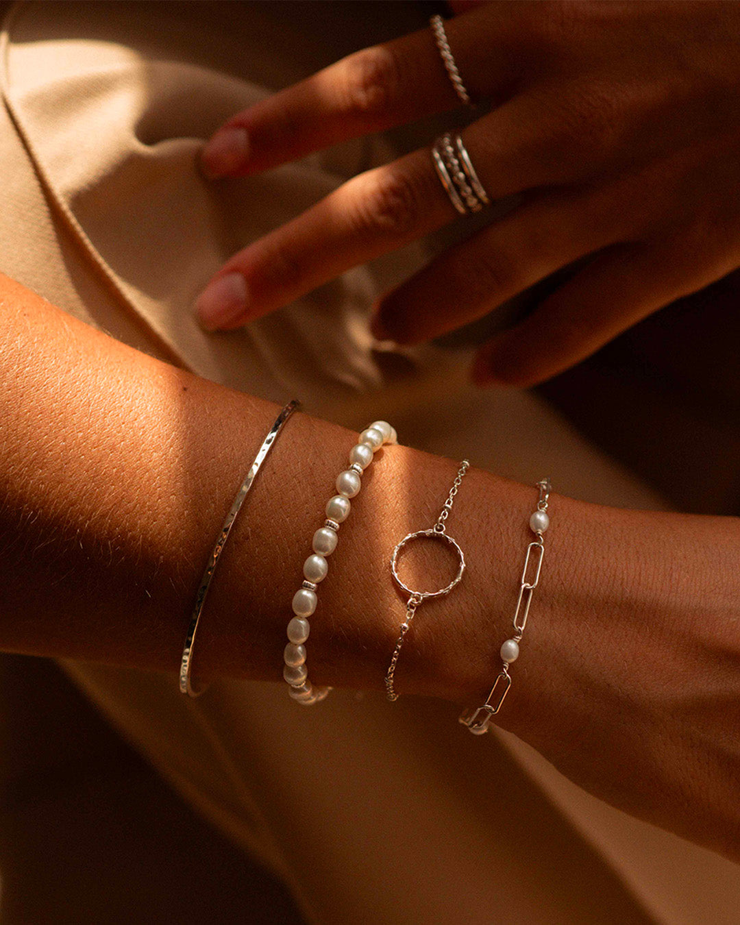 Association de bracelets en argent massif 925 composée d'un jonc fin martelé, d'un bracelet en perles de culture, d'un bracelet fin en chaîne boule avec un anneau en tige de fleur, et d'un bracelet en maille rectangle avec des perles de cultures rondes fabriqués en France.