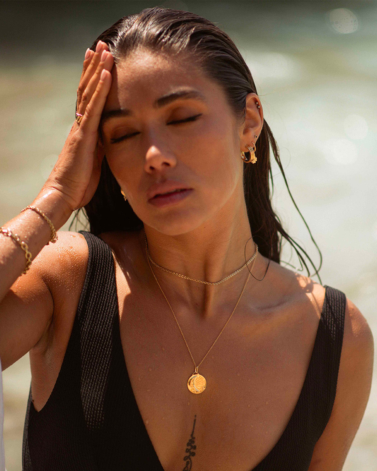 Association de bijoux éthiques composées d'un collier ras de cou en maille soleil, d'un collier en maille fine avec un pendentif en pièce large et une lune, d'une créole large au motif rayure, d'une boucle pendante avec un anneau et un trèfle, et d'une petite puce avec un pierre éthique noir en plaqué or 3 microns et made in France.