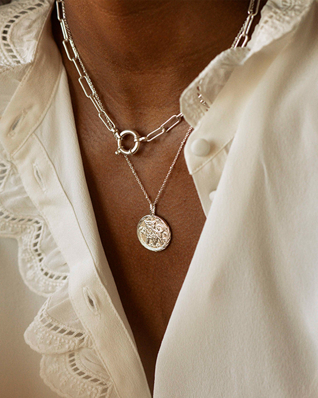 Association de bijoux éthiques fabriqués en France composée d'un collier en chaîne rectangle avec un gros fermoir rond, et d'un collier fin avec un pendentif formant une médaille au signe astrologique.