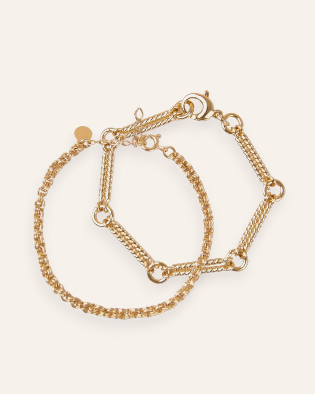 Composition de deux bracelets, avec un bracelet en chaîne tige torsadée accompagnée de mailles rondes, et  un bracelet en chaîne forçat avec des mailles rondes épaisses en plaqué or 18 carats.