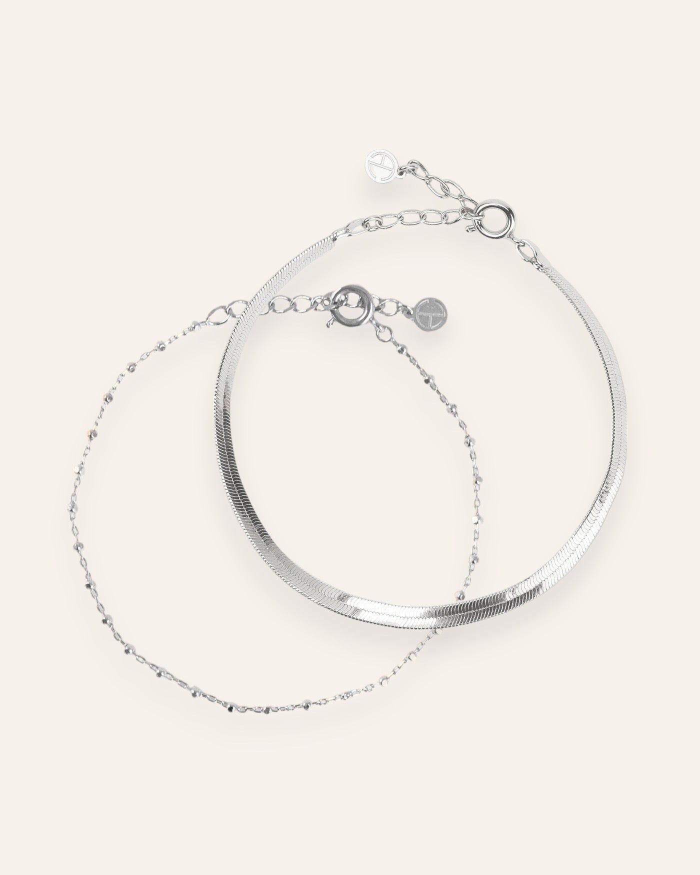 Composition de deux bracelets, avec un bracelet en chaîne fine habillée de petites mailles carrées, et un bracelet en chaîne plate en argent massif 925.