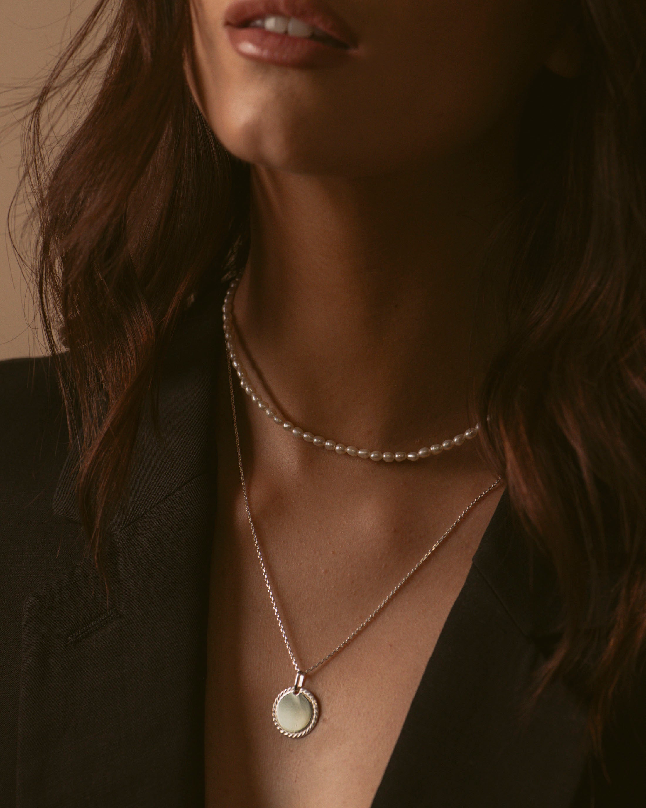 Association de deux colliers en argent massif 925, composée d'un collier full perles de culture, et un collier en chaîne forçat avec une médaille aux contours torsadés, fabriqués en France.