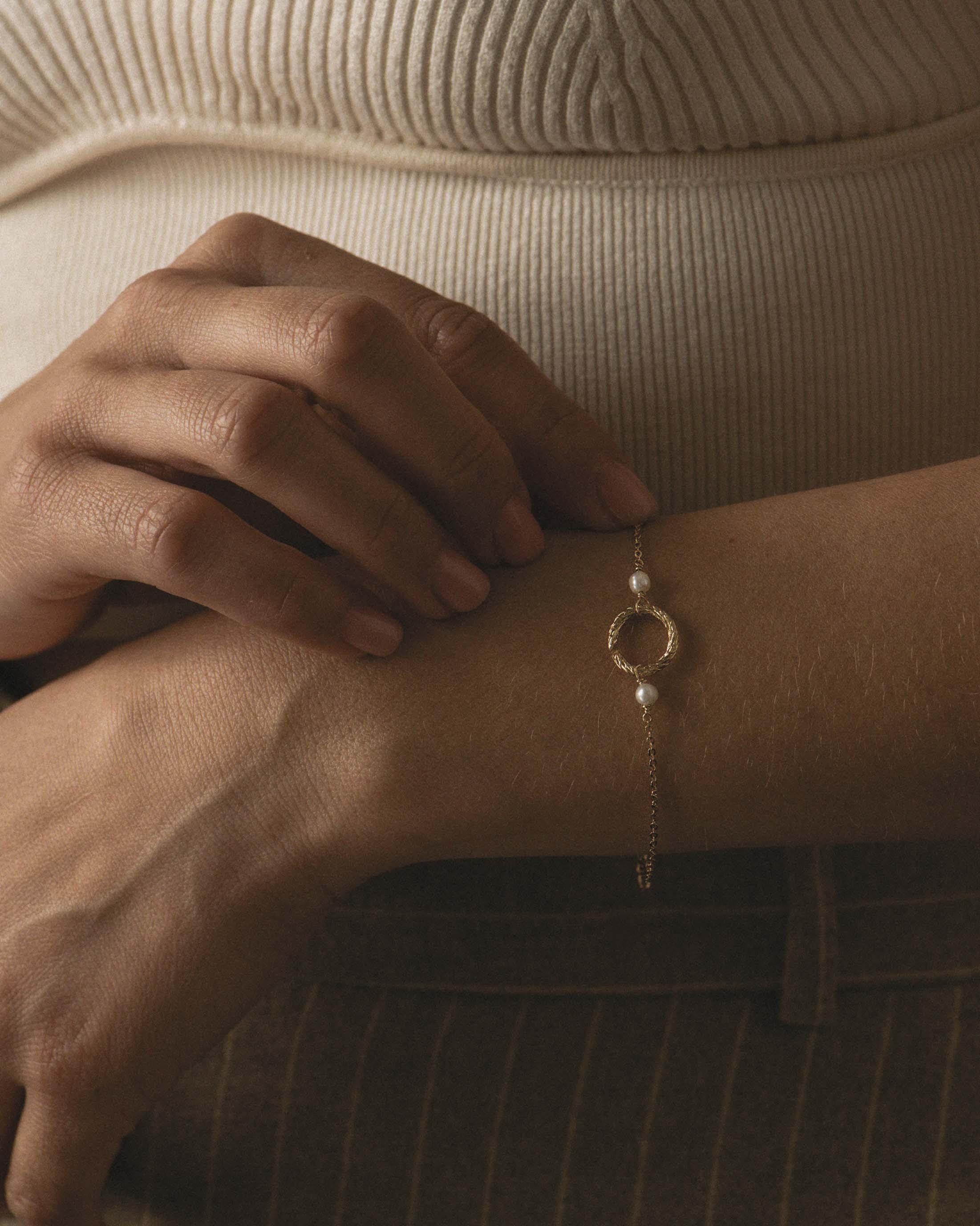Bracelet fin en plaqué or composé d'un anneau au motif rayé et de deux perles de cultures rondes fabriqué en France.