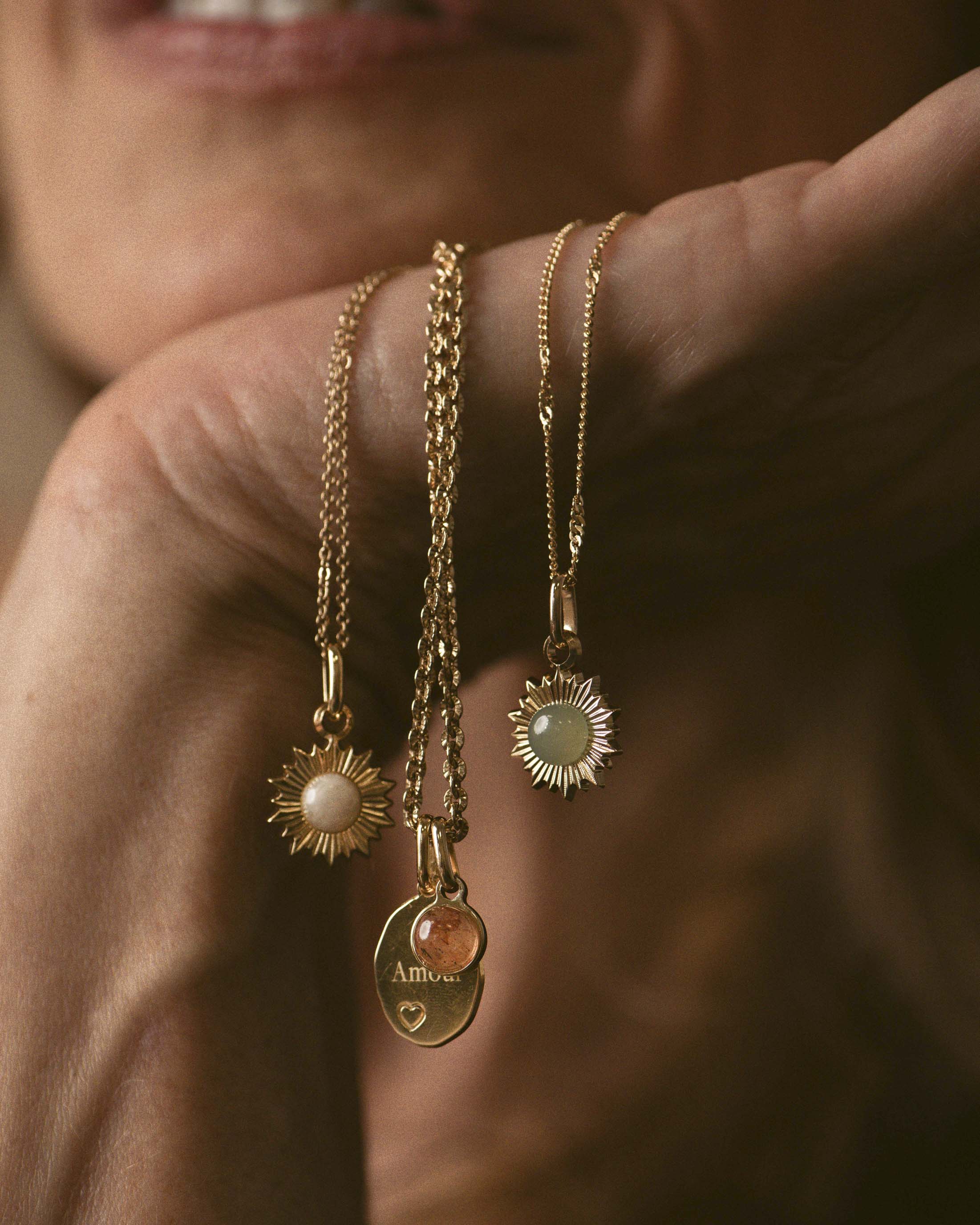 Association de colliers en plaqué or 18 carats, composée d'un collier en maille soleil avec une médaille ovale gravable au motif cœur associée à une pampille, et de deux autres colliers avec un pendentif soleil orné d'une pierre naturelle, fabriqués en France.