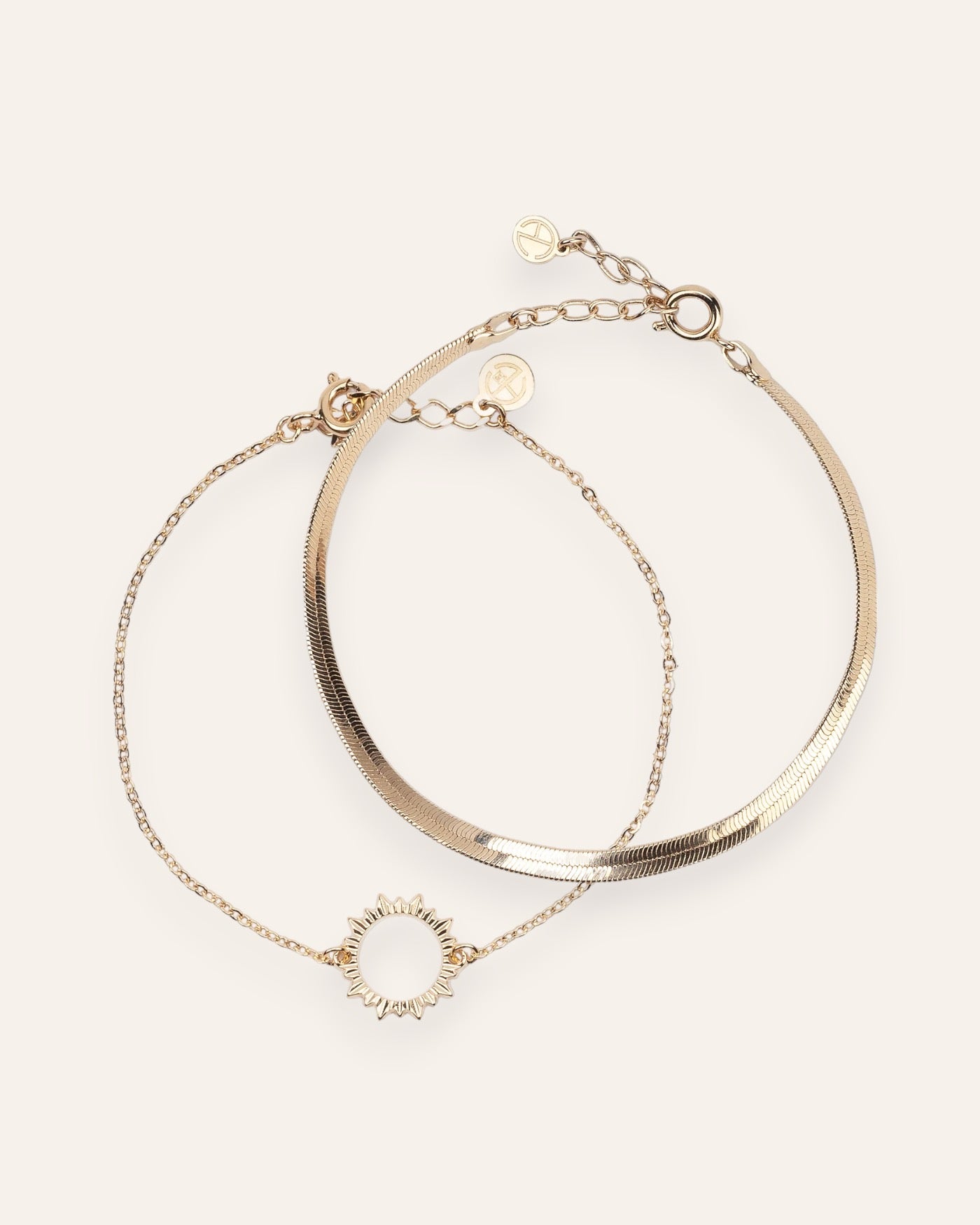 Composition de deux bracelets, avec un bracelet en chaîne fine habillé d'un soleil ajouré, et un bracelet en chaîne plate en plaqué or 18 carats.