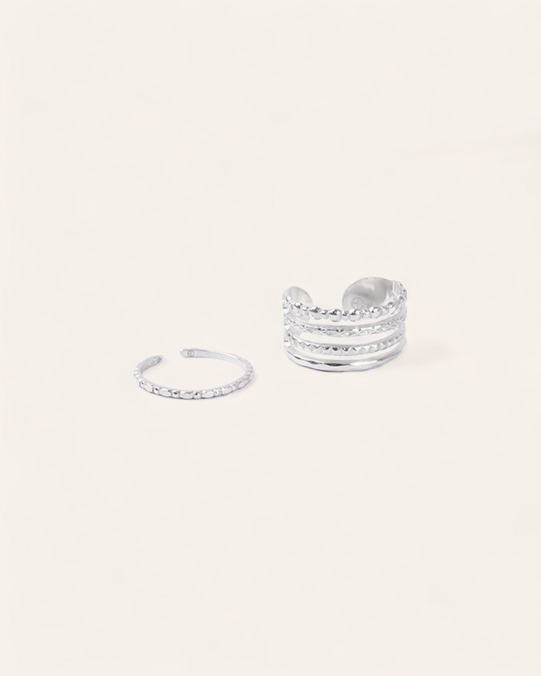 Composition de deux bagues ajustables avec une bague fine avec des petits motifs ronds, et une bague large avec deux anneaux lisses et un anneau avec un design formant plusieurs petits ronds, en argent massif 925.