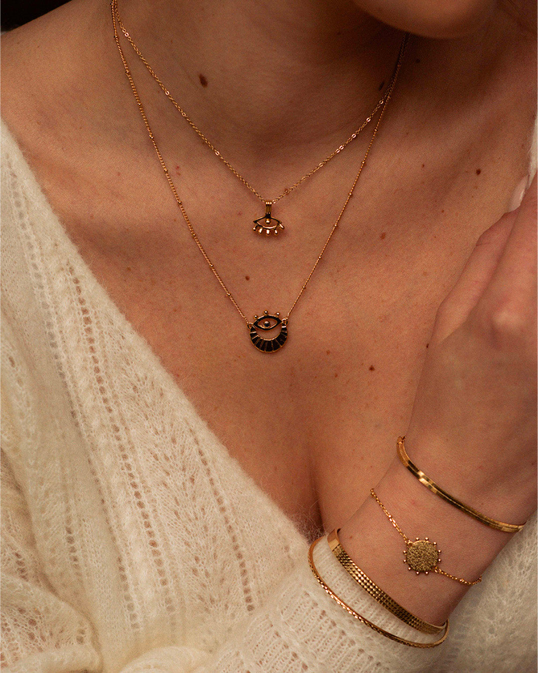 Association de bijoux en plaqué or 3 microns composée d'un collier fin avec un pendentif 3ème œil, d'un collier en chaîne boule avec un pendentif 3ème œil avec une demie lune, d'un bracelet en chaîne plate, d'un bracelet avec une estampe martelée ornée de petites boules, un jonc large ajustable martelé de deux rangées de petits carrés et d'un jonc fin fabriqués en France.