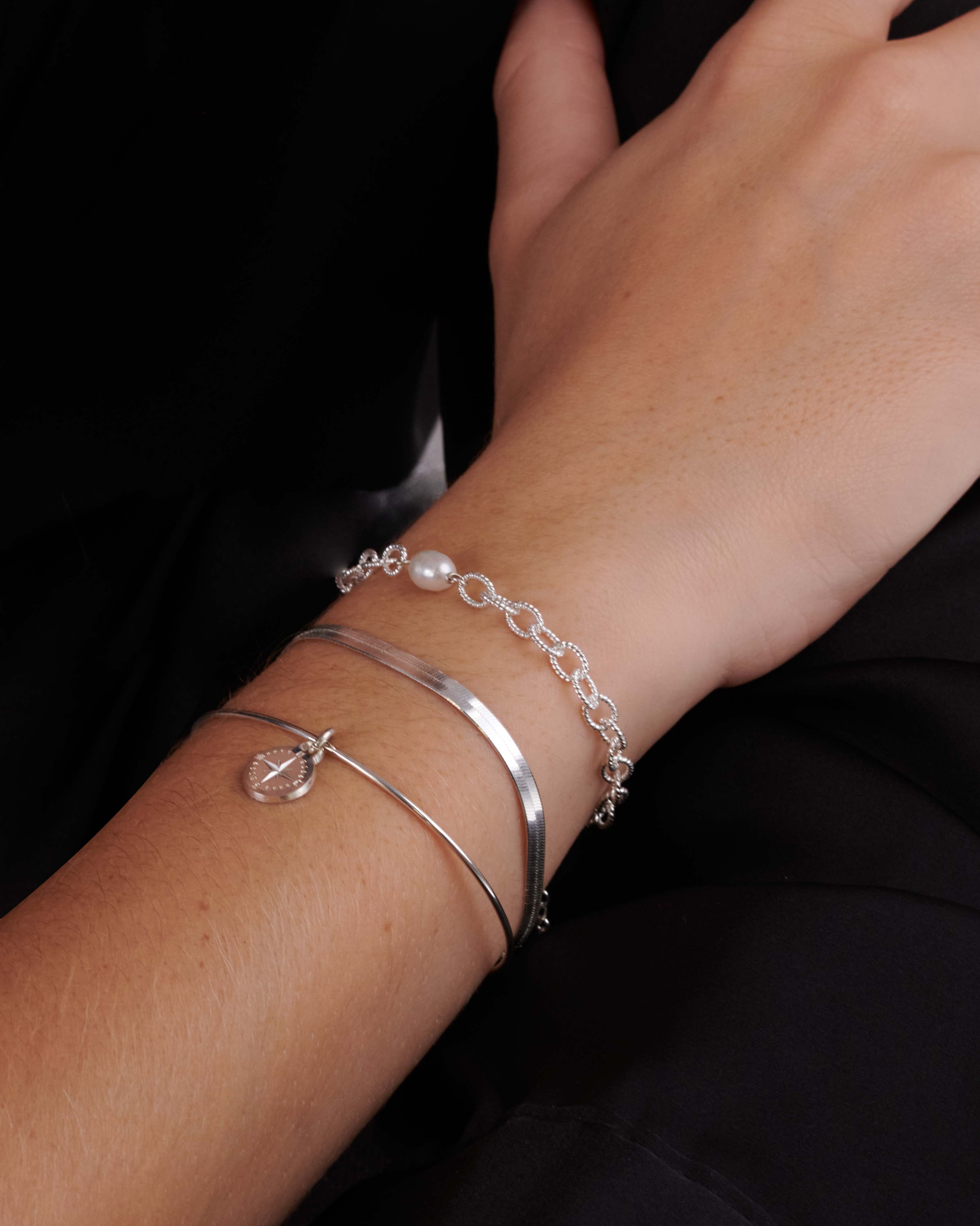 Association de bracelets éthiques en argent massif 925 composée d'un bracelet en chaîne ovale martelée avec une perle de culture ovale, d'un bracelet en chaîne plate, et d'un jonc fin avec un pendentif en rose des vents fabriqués en France.