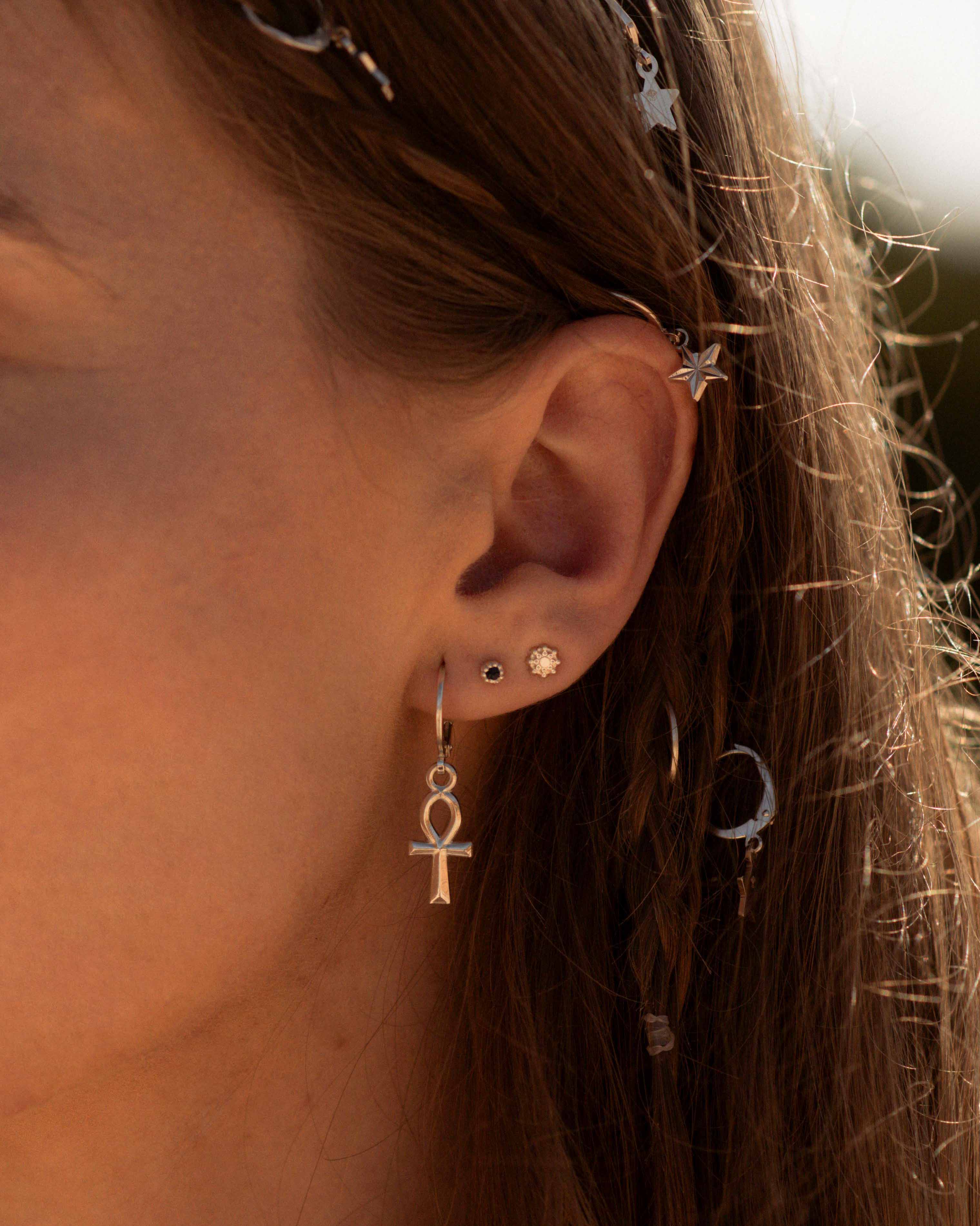 Association de boucles d'oreilles en argent massif 925, composée d'une dormeuse en croix égyptienne, d'une petite puce en onyx, et d'une petite puce au design soleil, fabriquées en France.